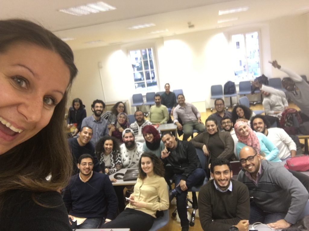 A group of people posing for a photo in a classroom, representing the startup support community.