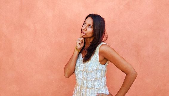 A woman in a white dress leveraging startup resources poses against a pink wall.