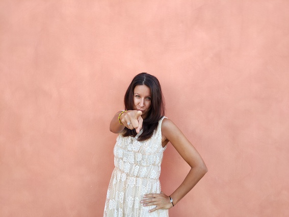A woman in a white dress pointing at a pink wall, providing marketing support for startups.