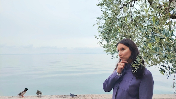 An entrepreneur wearing a purple jacket stands near a body of water, seeking startup support in the vibrant startup community.