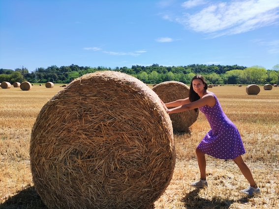 A woman utilizing entrepreneurial support while pushing a large hay bale in a field.