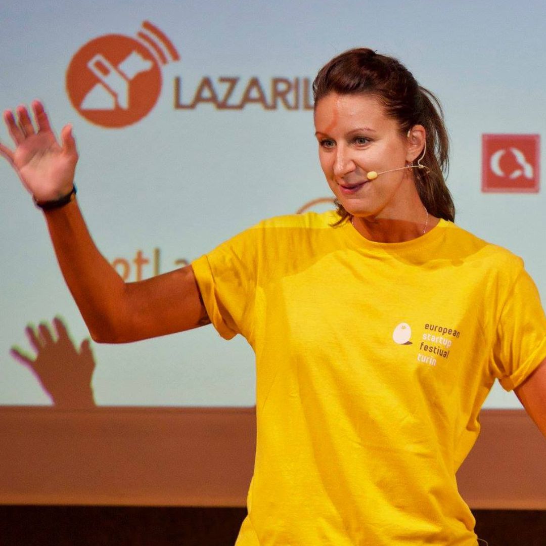 A woman in a yellow t-shirt delivering a speech at a startup community event, providing marketing support to aspiring entrepreneurs.