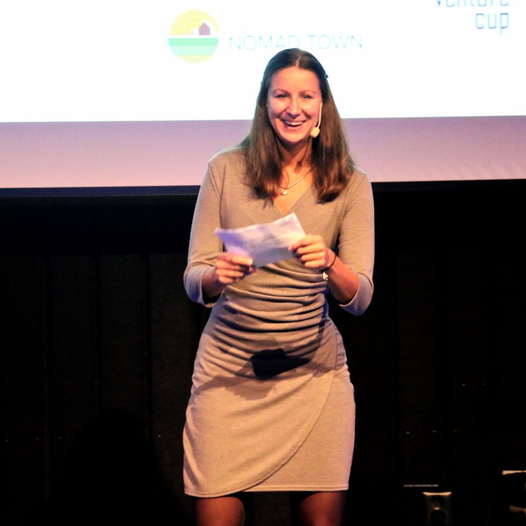 A woman standing on stage holding a piece of paper, offering startup support to the entrepreneurial community.