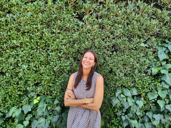 A startup coach supporting a woman in a striped dress standing in front of a hedge.