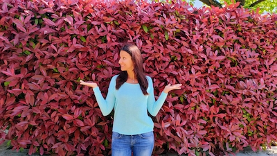 A woman receiving startup support posing in front of a red hedge.
