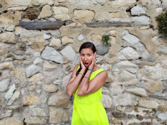 A woman in a yellow dress is posing gracefully in front of a stone wall.