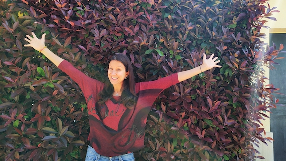 A woman standing in front of a wall with her arms outstretched, showcasing her expertise as a marketing coach in the vibrant startup community.