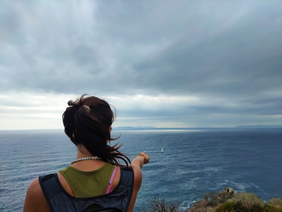 A woman pointing at the ocean with a backpack seeking startup coach support.