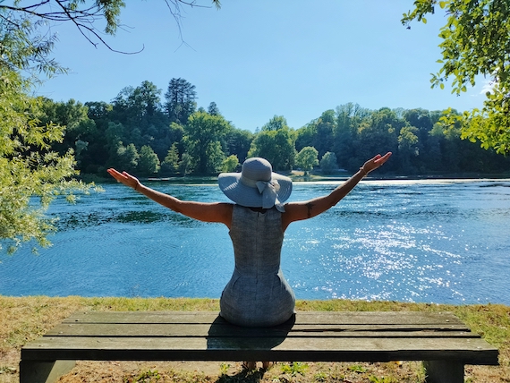 A woman sitting on a bench next to a river enjoying the peaceful scenery with her arms outstretched.