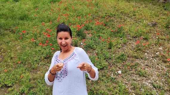 A woman posing in a field of blooming red flowers, receiving marketing support.