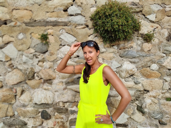 A woman in a yellow jumpsuit posing in front of a stone wall, seeking startup support and marketing guidance.