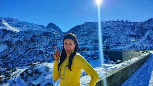 A woman posing for a photo in front of a snowy mountain, receiving marketing support from a marketing coach.