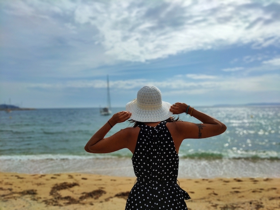A woman wearing a polka dot dress and a white hat enjoying the beach.
