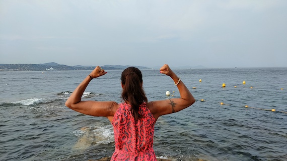 A strong woman flexing her muscles in front of the ocean, symbolizing the entrepreneurial spirit and the immense support of the startup community.