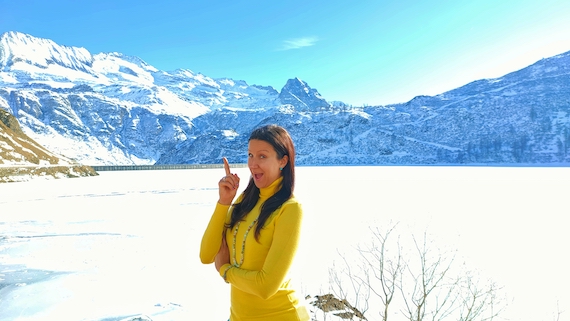 A woman in a yellow dress standing in front of a snow covered mountain, embracing the beauty of nature.