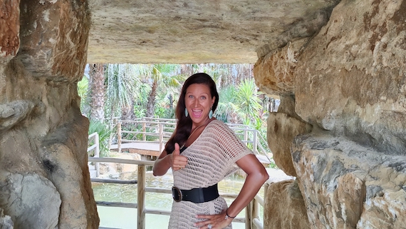 A woman standing in a cave, giving a thumbs up, surrounded by an entrepreneurial community offering marketing support.