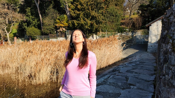 A woman in a pink shirt standing next to a pond, receiving startup coach support.