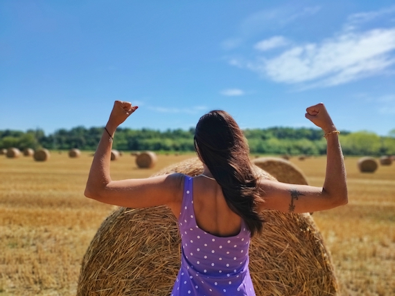 A woman is standing in a field with hay bales, receiving marketing support from a startup coach.